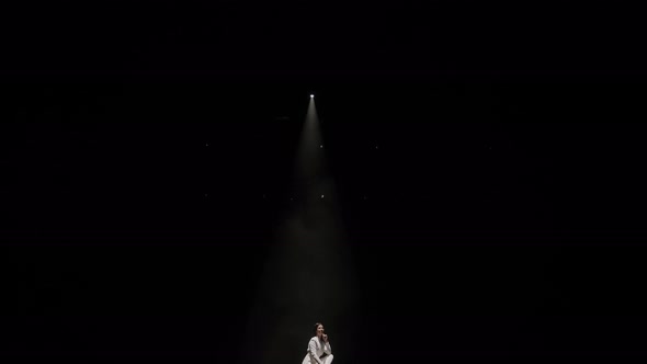 Portrait of a Woman in a White Suit on Stage in the Dark