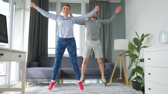 Caucasian Couple is Doing Jumping Jacks Exercise at Home in Cozy Bright Room Slow Motion