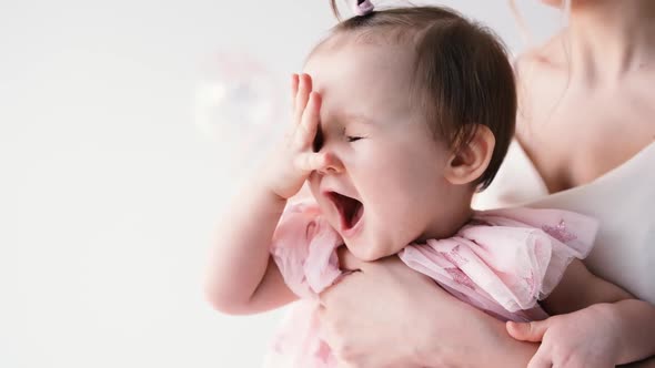 Cute Little Girl in a Birthday Dress in Her Mother's Arms Fooling Around and Smiling