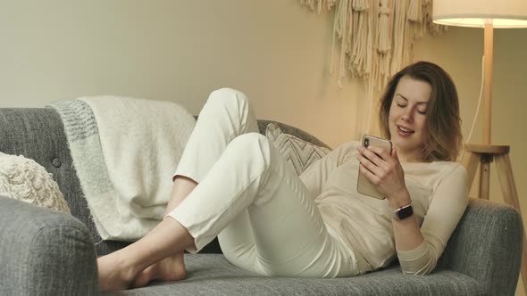 Bare Feet Female Sits on Sofa with Phone in Hands