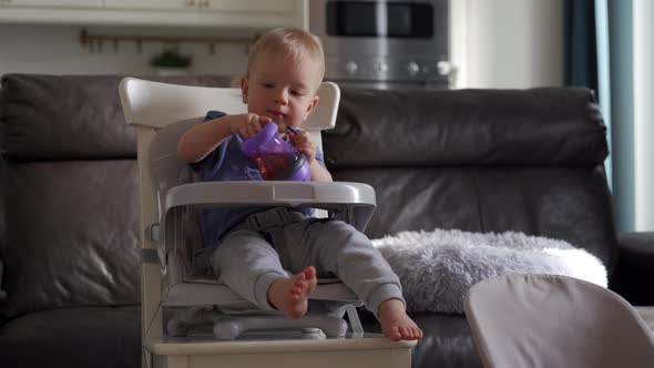 Cute Kid with Baby Straw Feeding Cup Sitting in Booster Seat One Year Old Toddler Watching Tv