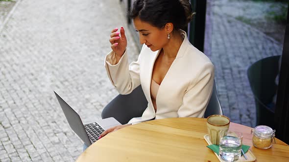 Young Smiling Brunette Business Woman in Stylish Smart Dress Working on Laptop in Cafe at Street of