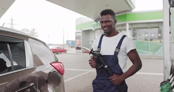 Black African Gas Station Worker Holding a Pistol to Refuel a Car