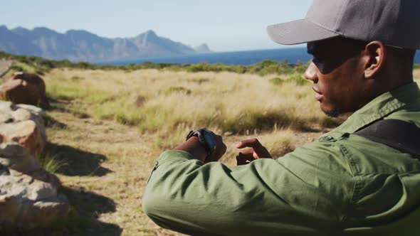 African american man hiking in countryside by the coast using smartwatch