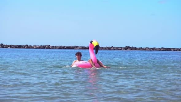 Young Male Swimming on Pink Inflatable Flamingo on Summer Sea