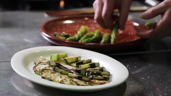 Close up of hands plating asparagus and zucchinis in a clay plateau, preparing a vegetarian green sa