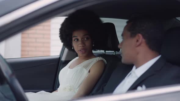Smiling African American Bride Sitting on Passenger Seat Talking with Groom on Driver's Seat in Car