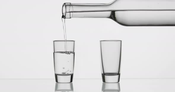 Pouring Up Two Shot of Vodka From a Bottle Into Glass. White Background