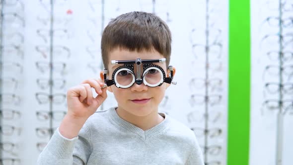 The Boy Stands on a Background of a Showwindow with Frames for Spectacles with the Device 