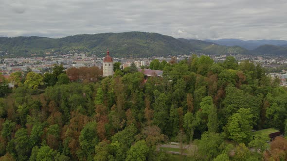 Aerial view flying away from Graz's Schloßberg hilltop woodland park and Glockenturm tower