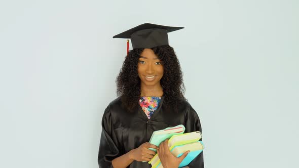 A Young African American Woman in a Black Robe and a Master's Hat Stands Straight Holding Textbooks