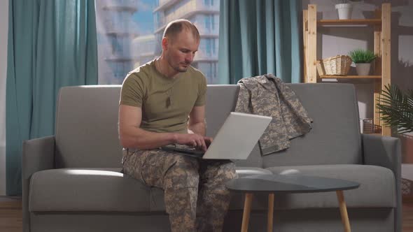 Professional Military Man Sits on a Sofa with a Living Room at Home and Uses a Notebook