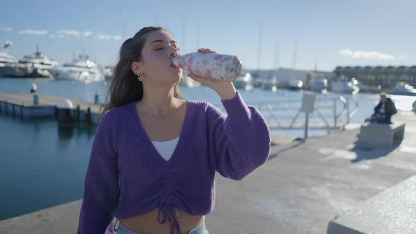 Teenage Girl Drinks Out of Bottle By Harbor in Sunlight Close Slomo