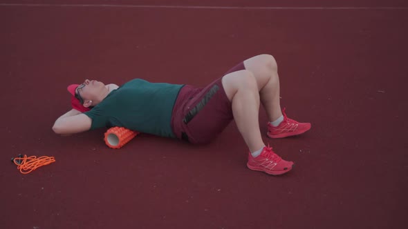 Woman Stretching Back Muscles on Orange Foam Roller at Outdoor Gym After Wokout