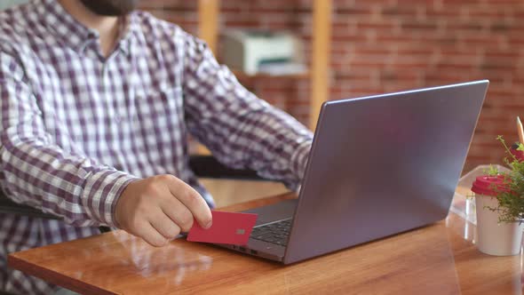 Man is Sitting with Debit Card Front of Laptop Filling Out Information for Buying or Getting Help