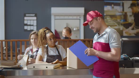 Delivery Man with Clipboard Talking To Waitress About Take Away Order in Cafeteria