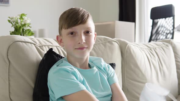 A Young Boy Takes Off a Face Mask and Looks at the Camera As He Sits on a Couch at Home - Closeup