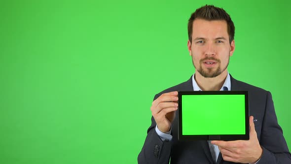 A Young Businessman Talks To the Camera and Holds Out a Tablet with Green Screen - Green Screen