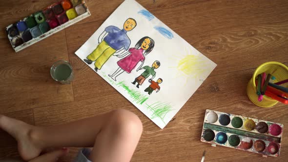 A Child Paints a Drawing on the Floor with Watercolors