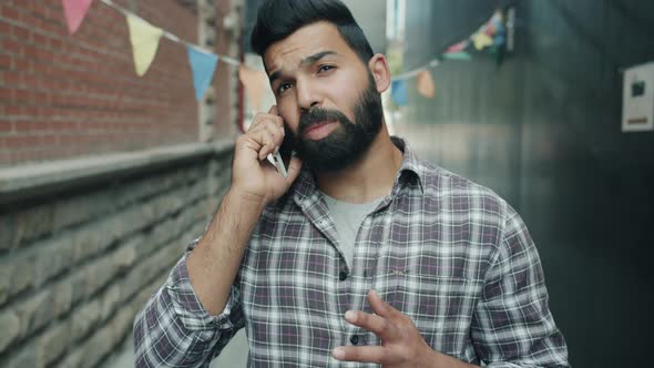 Portrait of Attractive Arab Guy Chatting on Mobile Phone and Gesturing Standing Alone in Street