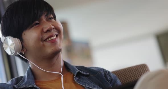 Happy young Asian man listening for music with headphone in living room.