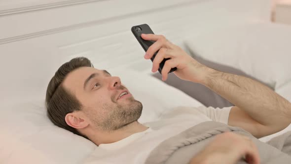 Video Chat on Smartphone By Young Man Laying in Bed