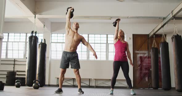 Fit caucasian woman and man working out with kettle bells at the gym