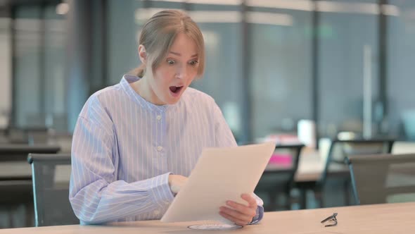 Young Woman Celebrating Success While Reading Documents in Office