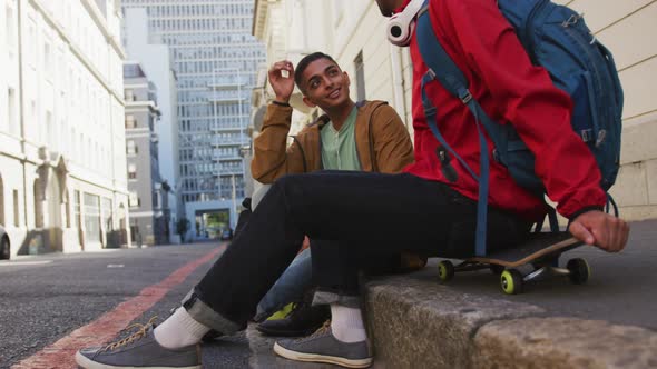 Two happy mixed race male friends sitting and talking in the street