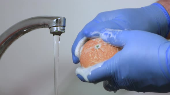 Male Hands in Gloves Closeup Wash Tangerine with Soap and Water