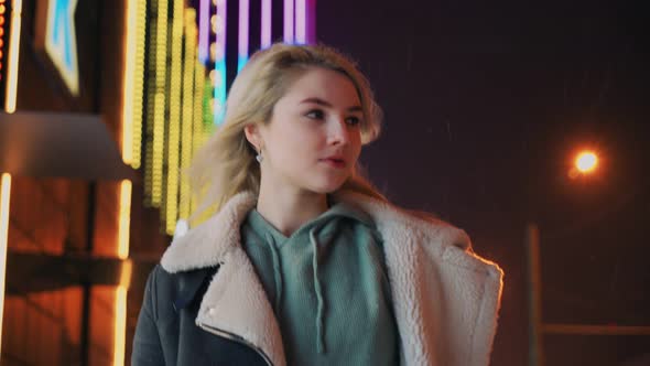 Lonely Girl Walking on Winter Night During Snowfall Near Glowing Shopping Mall