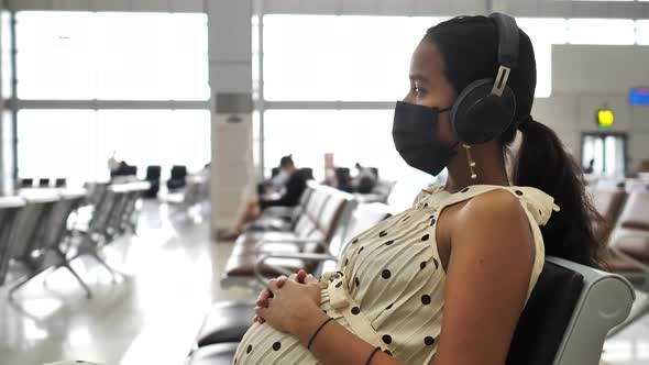 Pregnant Woman Weating Mask and Headset Sitting in Airpot Waiting Area