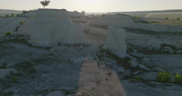 pedestal aerial shot of man running between two cliffs, with a lonely tree on top of one of it