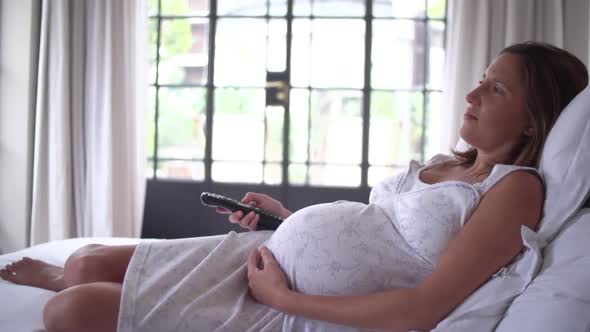 Pregnant woman lying on bed, watching TV