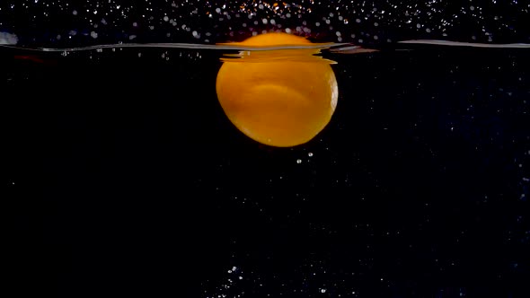 Vibrant orange being dropped into water in slow motion.