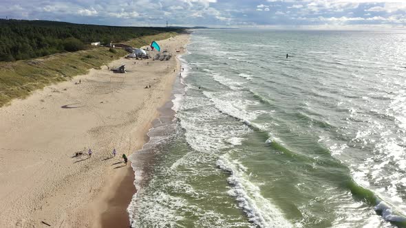 AERIAL: People Walking on a Beach with Surfer Surfing Alongside Baltic Sea Beach