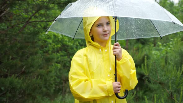 Cute Girl in Yellow Raincoat Holds Umbrella on Rainy Day