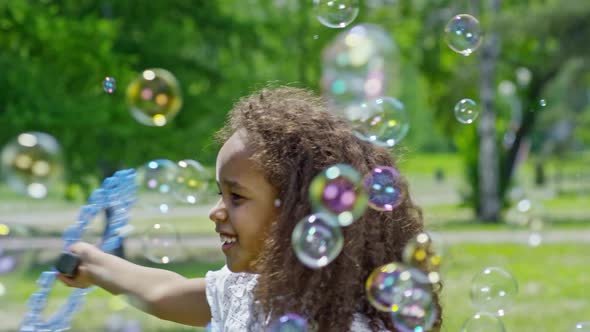 Playful Little African Girl Making Bubbles in Park alt
