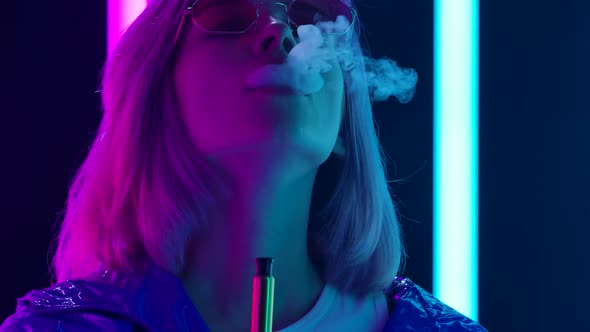 Portrait of a Young Stylish Woman in Sunglasses Smoking a Hookah and Blowing Out Puffs of Smoke