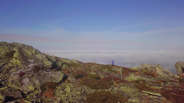 Aerial View of Unrecognizable Person Hiking Along Rocky Mountain Ridge Above Clouds at High Altitude