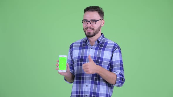 Happy Young Bearded Hipster Man Showing Phone and Giving Thumbs Up