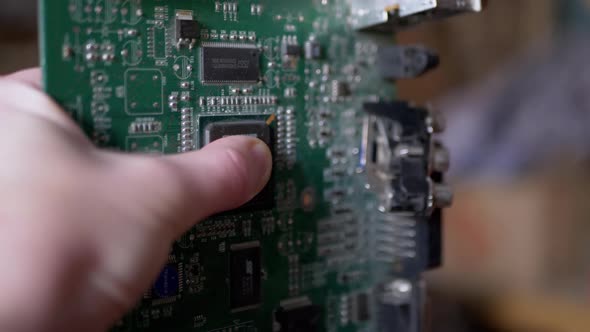 Female Hand Rotates Old Printed Circuit Board with Chip with Conductive Tracks