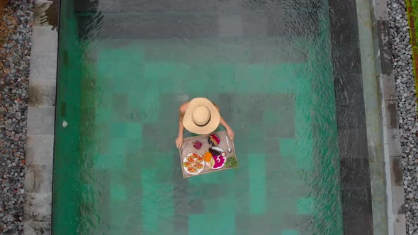 Aerial Shot of a Young Woman Tourist Has Her Own Personal Breakfast on a Floating Table