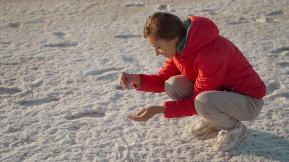 Woman in Red Jacket Smiling and Holding Salt Crystals in Hands at Beautiful Landscape of Salt Flats