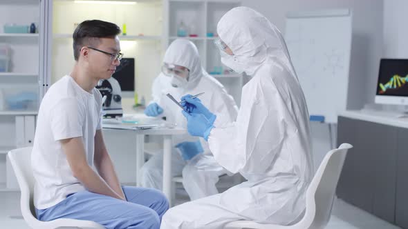 Doctor in Disposable Coveralls Writing down Patients Symptoms