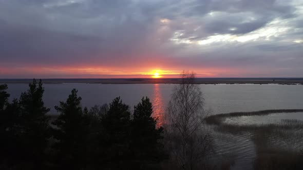 Aerial Drone footage of rising out of a forest to a view of sunset over a lake