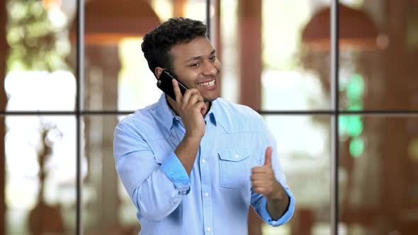 Happy Emotional Brownskinned Man Talking on Phone in Restaurant