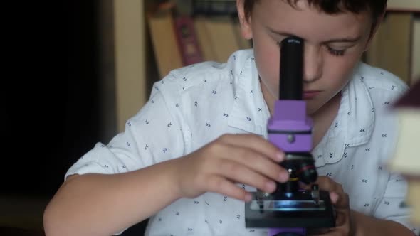 the boy Looks through the microscope. Rubs his hands over his eyes from fatigue