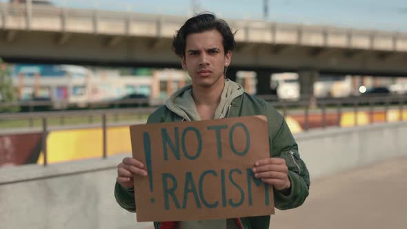 Young Guy Standing on City Street with No to Racism Banner