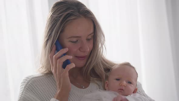 Closeup Smiling Happy Caucasian Mother Talking on Phone Holding Infant Daughter in Hands